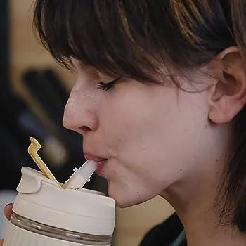 Person drinking from a white tumbler with a straw in a blurred indoor setting
